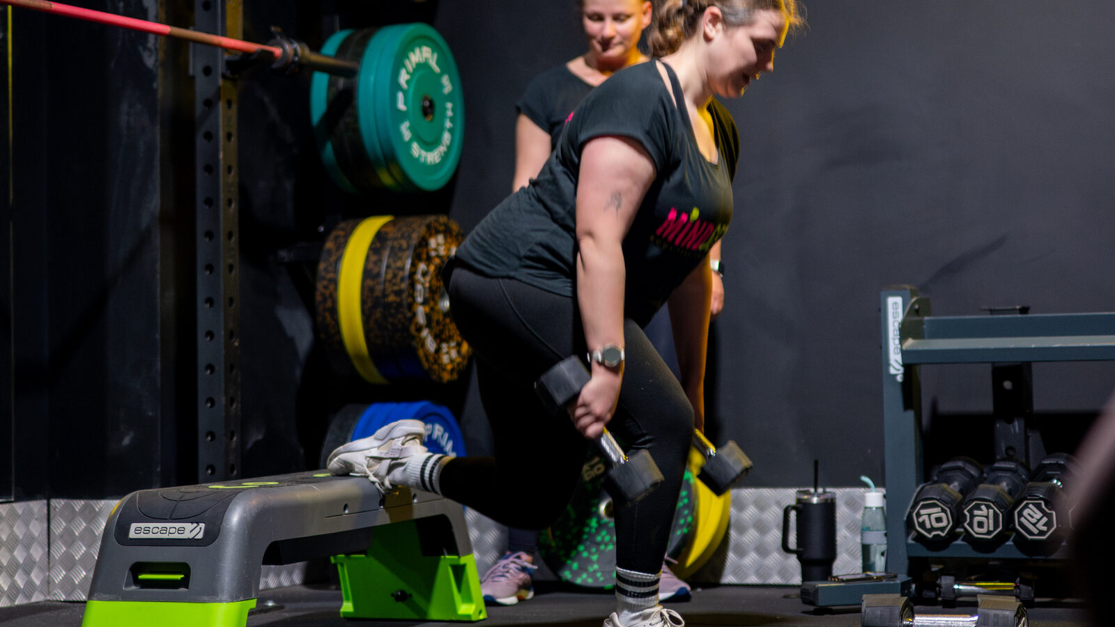 A Mindset member lifting dumbbells during a small-group session, with her coach watching close by